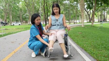 Tekerlekli sandalyede oturan ve parkta kadın bir hemşire tarafından bakılan yaşlı bir kadın. Doğal terapi konsepti. Ya da yaşlıların bakıcıları.