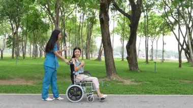 Tekerlekli sandalyede oturan ve parkta kadın bir hemşire tarafından bakılan yaşlı bir kadın. Doğal terapi konsepti. Ya da yaşlıların bakıcıları.