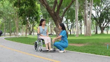 Tekerlekli sandalyede oturan ve parkta kadın bir hemşire tarafından bakılan yaşlı bir kadın. Doğal terapi konsepti. Ya da yaşlıların bakıcıları.