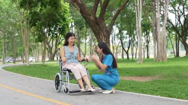 Tekerlekli sandalyede oturan ve parkta kadın bir hemşire tarafından bakılan yaşlı bir kadın. Doğal terapi konsepti. Ya da yaşlıların bakıcıları.