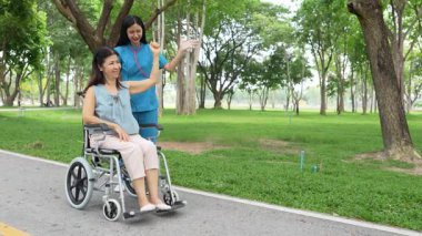 Tekerlekli sandalyede oturan ve parkta kadın bir hemşire tarafından bakılan yaşlı bir kadın. Doğal terapi konsepti. Ya da yaşlıların bakıcıları.