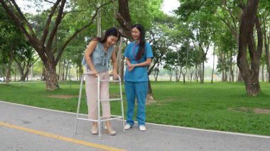 Genç bir Asyalı doktor yaşlı bir kadını parkta yürüyüşe çıkarıyor. Doğal terapi konsepti. Yaşlıların bakıcısı veya çalışanı.