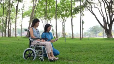 Tekerlekli sandalyede oturan ve parkta kadın bir hemşire tarafından bakılan yaşlı bir kadın. Doğal terapi konsepti. Ya da yaşlıların bakıcıları.