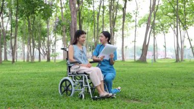 Tekerlekli sandalyede oturan ve parkta kadın bir hemşire tarafından bakılan yaşlı bir kadın. Doğal terapi konsepti. Ya da yaşlıların bakıcıları.