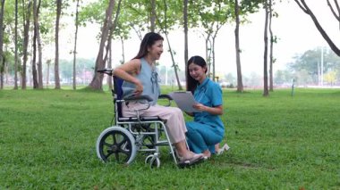 Tekerlekli sandalyede oturan ve parkta kadın bir hemşire tarafından bakılan yaşlı bir kadın. Doğal terapi konsepti. Ya da yaşlıların bakıcıları.