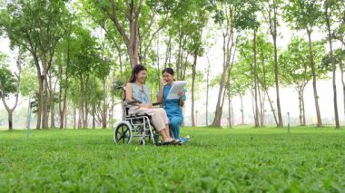 Tekerlekli sandalyede oturan ve parkta kadın bir hemşire tarafından bakılan yaşlı bir kadın. Doğal terapi konsepti. Ya da yaşlıların bakıcıları.