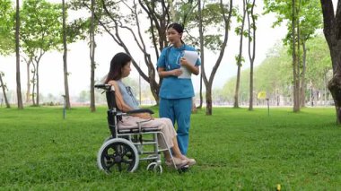 Tekerlekli sandalyede oturan ve parkta kadın bir hemşire tarafından bakılan yaşlı bir kadın. Doğal terapi konsepti. Ya da yaşlıların bakıcıları.