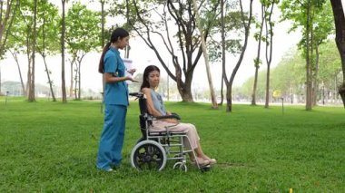 Tekerlekli sandalyede oturan ve parkta kadın bir hemşire tarafından bakılan yaşlı bir kadın. Doğal terapi konsepti. Ya da yaşlıların bakıcıları.