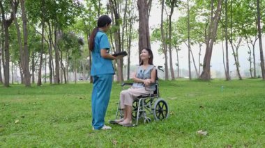 Tekerlekli sandalyede oturan ve parkta kadın bir hemşire tarafından bakılan yaşlı bir kadın. Doğal terapi konsepti. Ya da yaşlıların bakıcıları.