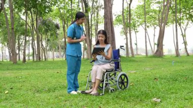 Tekerlekli sandalyede oturan ve parkta kadın bir hemşire tarafından bakılan yaşlı bir kadın. Doğal terapi konsepti. Ya da yaşlıların bakıcıları.