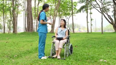 Tekerlekli sandalyede oturan ve parkta kadın bir hemşire tarafından bakılan yaşlı bir kadın. Doğal terapi konsepti. Ya da yaşlıların bakıcıları.