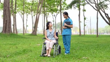 Tekerlekli sandalyede oturan ve parkta kadın bir hemşire tarafından bakılan yaşlı bir kadın. Doğal terapi konsepti. Ya da yaşlıların bakıcıları.