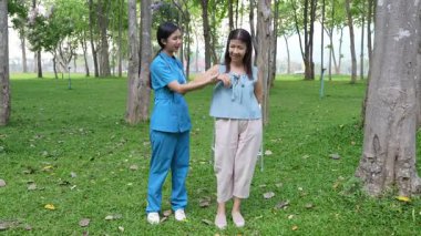 Genç bir Asyalı doktor yaşlı bir kadını parkta yürüyüşe çıkarıyor. Doğal terapi konsepti. Yaşlıların bakıcısı veya çalışanı.