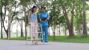 Genç bir Asyalı doktor yaşlı bir kadını parkta yürüyüşe çıkarıyor. Doğal terapi konsepti. Yaşlıların bakıcısı veya çalışanı.