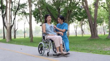 Tekerlekli sandalyede oturan ve parkta kadın bir hemşire tarafından bakılan yaşlı bir kadın. Doğal terapi konsepti. Ya da yaşlıların bakıcıları.