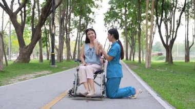 Tekerlekli sandalyede oturan ve parkta kadın bir hemşire tarafından bakılan yaşlı bir kadın. Doğal terapi konsepti. Ya da yaşlıların bakıcıları.