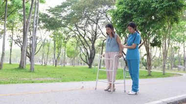 Genç bir Asyalı doktor yaşlı bir kadını parkta yürüyüşe çıkarıyor. Doğal terapi konsepti. Yaşlıların bakıcısı veya çalışanı.