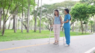 Genç bir Asyalı doktor yaşlı bir kadını parkta yürüyüşe çıkarıyor. Doğal terapi konsepti. Yaşlıların bakıcısı veya çalışanı.