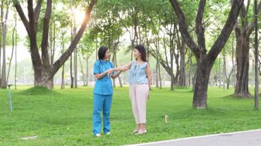Genç bir Asyalı doktor yaşlı bir kadını parkta yürüyüşe çıkarıyor. Doğal terapi konsepti. Yaşlıların bakıcısı veya çalışanı.