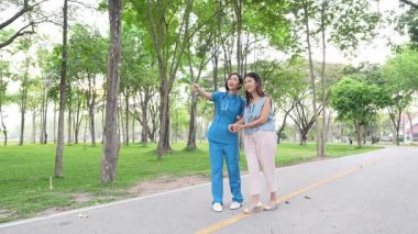 Genç bir Asyalı doktor yaşlı bir kadını parkta yürüyüşe çıkarıyor. Doğal terapi konsepti. Yaşlıların bakıcısı veya çalışanı.