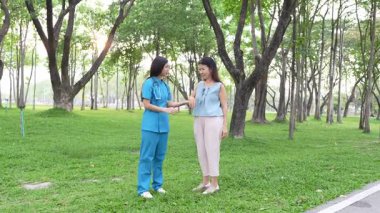 Genç bir Asyalı doktor yaşlı bir kadını parkta yürüyüşe çıkarıyor. Doğal terapi konsepti. Yaşlıların bakıcısı veya çalışanı.
