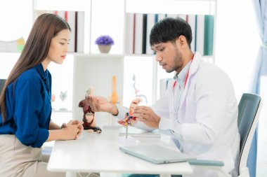 Orta yaşlı bir erkek doktor, klinikte bir kadın hastaya teşhis koyarken kemik ağrılarını anlatıyor ve klinikte notlar alıyor..