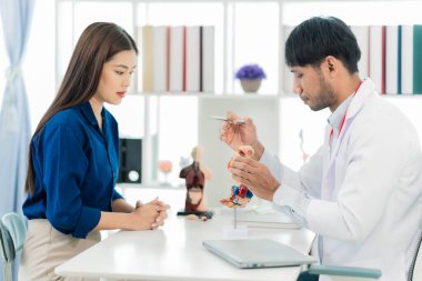 Orta yaşlı bir erkek doktor, klinikte bir kadın hastaya teşhis koyarken kemik ağrılarını anlatıyor ve klinikte notlar alıyor..