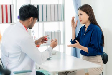 Orta yaşlı bir erkek doktor, klinikte bir kadın hastaya teşhis koyarken kemik ağrılarını anlatıyor ve klinikte notlar alıyor..