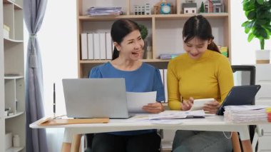 Yaşlı kadın ve Asyalı kadın evde muhasebe belgeleri üzerinde birlikte çalışıyorlar. Anne bilgisayarın nasıl kullanılacağını öğreniyor ya da evdeki kızından internet üzerinden teknoloji bilgisi arıyor..