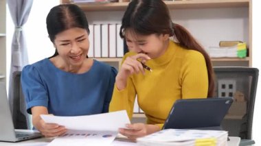 Yaşlı kadın ve Asyalı kadın evde muhasebe belgeleri üzerinde birlikte çalışıyorlar. Anne bilgisayarın nasıl kullanılacağını öğreniyor ya da evdeki kızından internet üzerinden teknoloji bilgisi arıyor..