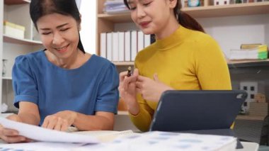 Yaşlı kadın ve Asyalı kadın evde muhasebe belgeleri üzerinde birlikte çalışıyorlar. Anne bilgisayarın nasıl kullanılacağını öğreniyor ya da evdeki kızından internet üzerinden teknoloji bilgisi arıyor..