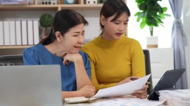 Yaşlı kadın ve Asyalı kadın evde muhasebe belgeleri üzerinde birlikte çalışıyorlar. Anne bilgisayarın nasıl kullanılacağını öğreniyor ya da evdeki kızından internet üzerinden teknoloji bilgisi arıyor..