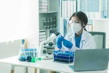 Laboratuar laboratuarında mikroskop deneyi sırasında plastik şişeden deney kabına mavi sıvı kimyasal döken laboratuvar önlüklü kadın doktor..