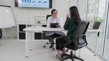 Orta yaşlı Asyalı erkek doktor klinikteki kadın hastanın tıbbi sonuçlarını kontrol ediyor, profesyonel sağlık danışmanlığı sırasında hastayla tıbbi sorunları tartışıyor.