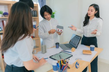 Genç Asyalı mimarlardan oluşan bir ekip, ofis, takım çalışması ve sanayi konsepti üzerinde çalışma planları ve inşaat araçları kullanarak yeni bir proje planlıyor..