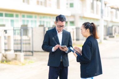 Proje yöneticisi, köy emlak şirketindeki yol yapım çalışmalarının ilerlemesini kontrol etmek için asistanına danışıyor..