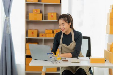 Genç Asyalı kız evde kendi işi olan bir serbest çalışan. Dizüstü bilgisayarla çalışan genç kadın, KOBİ işine çevrimiçi satış, pazarlama, paketleme, teslimat, KOBİ ve e-ticaret konseptiyle başladı.