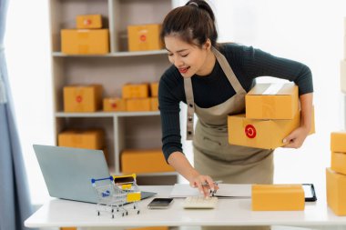 Genç Asyalı kız evde kendi işi olan bir serbest çalışan. Dizüstü bilgisayarla çalışan genç kadın, KOBİ işine çevrimiçi satış, pazarlama, paketleme, teslimat, KOBİ ve e-ticaret konseptiyle başladı.