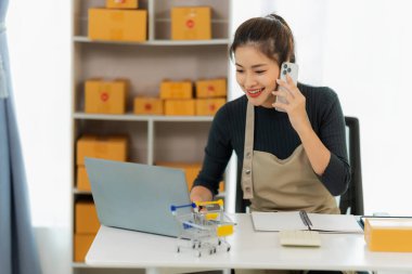 Genç Asyalı kız evde kendi işi olan bir serbest çalışan. Dizüstü bilgisayarla çalışan genç kadın, KOBİ işine çevrimiçi satış, pazarlama, paketleme, teslimat, KOBİ ve e-ticaret konseptiyle başladı.