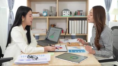 Birlikte çalışan iki Asyalı iş kadını kararlı ve profesyoneldir. Birlikte çalışırlar. Gülümser ve bilgisayarla ve tabletle belgeleri tartışırlar.