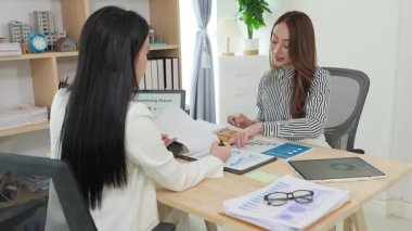 Birlikte çalışan iki Asyalı iş kadını kararlı ve profesyoneldir. Birlikte çalışırlar. Gülümser ve bilgisayarla ve tabletle belgeleri tartışırlar.