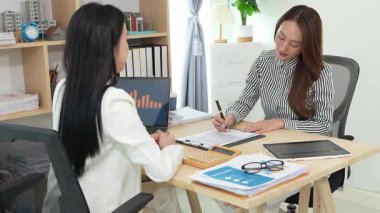 Birlikte çalışan iki Asyalı iş kadını kararlı ve profesyoneldir. Birlikte çalışırlar. Gülümser ve bilgisayarla ve tabletle belgeleri tartışırlar.