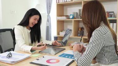 Birlikte çalışan iki Asyalı iş kadını kararlı ve profesyoneldir. Birlikte çalışırlar. Gülümser ve bilgisayarla ve tabletle belgeleri tartışırlar.