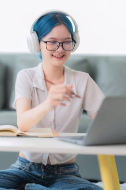 Kulaklık takan genç Asyalı bir kız öğrenci internette sohbet ederken kampüste ya da üniversitede dizüstü bilgisayar kullanarak uzaktan öğreniyor.