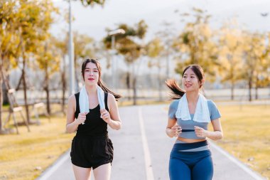 Spor elbiseli iki genç kadın parkta birlikte yürüyor, birlikte koşuyorlar..