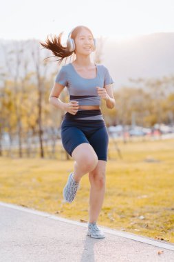 Parkta spor kıyafetleri içinde koşan güzel bir Asyalı kadın. Egzersiz konsepti, sağlıklı yaşam tarzı.