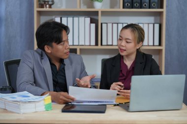 Resmi giyinmiş iki Asyalı iş adamı bir masada birlikte çalışıyor, gülümsüyor ve iş hakkında konuşuyorlar. Finansal tabloyu göster ve bir tablet ve dizüstü bilgisayarla bir ofis masasında işbirliği yap.