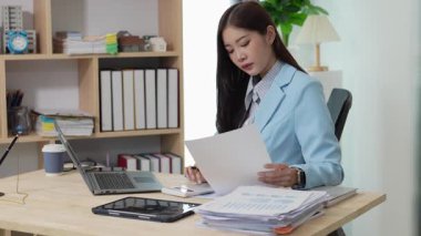 Bilgisayarı ve finansal belgeleri olan genç Asyalı kadın çalışanlar ofis masasında gülümsüyor ve grafikleri gösteren bilgisayarlarla çalışıyor. başlangıç iş fikri