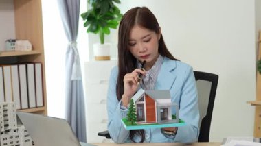 Asyalı bayan emlakçı müşterilere internet üzerinden danışmanlık hizmeti sunar müşteriye bir ev ya da dairenin içini tarif eder. Çevrimiçi ev satışı danışmanı