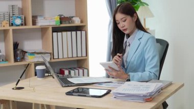 Bilgisayarı ve finansal belgeleri olan genç Asyalı kadın çalışanlar ofis masasında gülümsüyor ve grafikleri gösteren bilgisayarlarla çalışıyor. başlangıç iş fikri